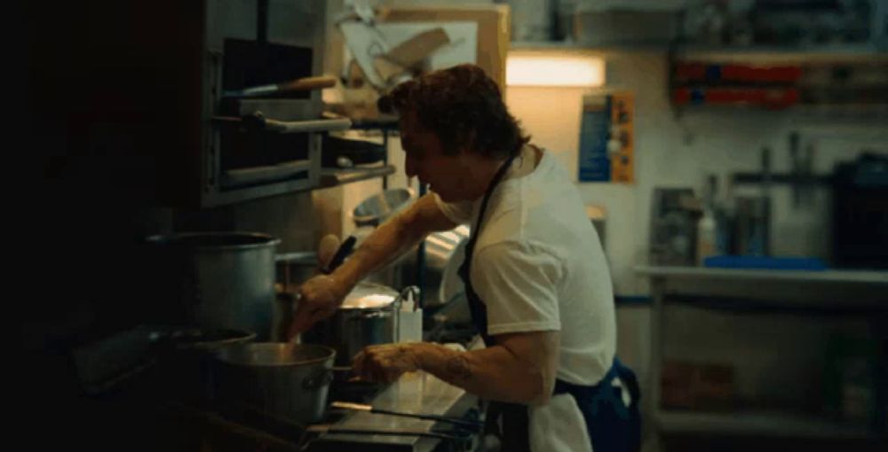 a man in an apron is cooking in a kitchen with a sign on the wall that says no smoking