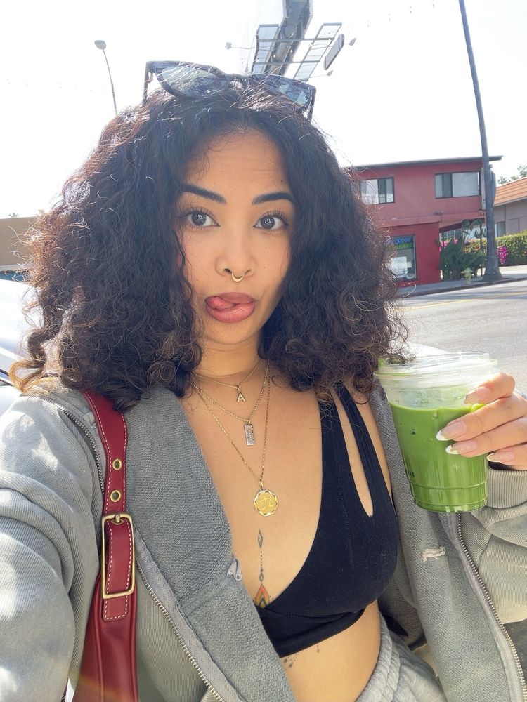 person with curly hair holding a matcha latte