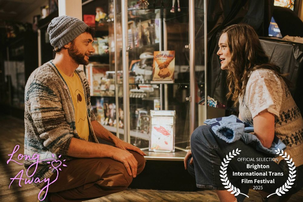 Justin Lawrence Barnes as Dad and Griffin Kelly as Victoria, talking in front of a display case full of comic books inside a comic shop, with the Long Away logo
official selection Brighton International Trans Film Festival 2025