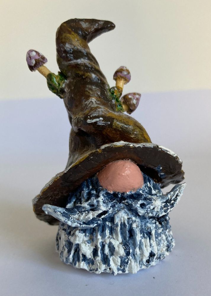A small, hand-painted clay model head of a wizard with no eyes visible and a big nose, a grey coloured mustache and beard, wearing a pointy hat with fungi growing out of it. This is the start of my author's journey.