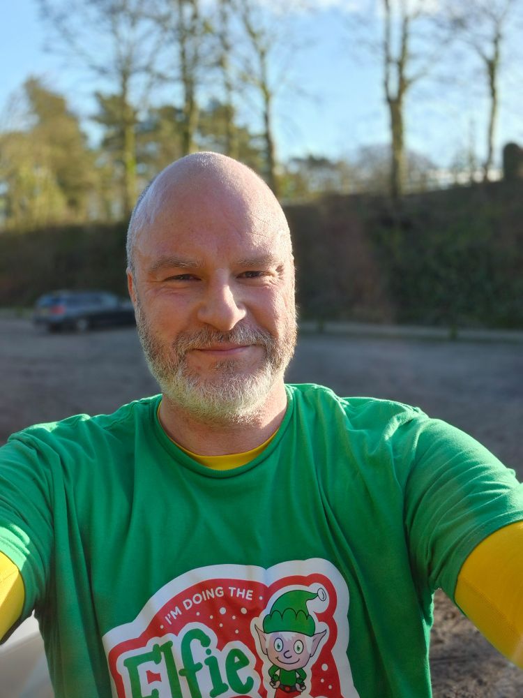 Me smiling in a selfie picture at the end of the run. I am wearing my bright green tshirt with elfie run on it, and a yellow base layer that you can see on my arms. 