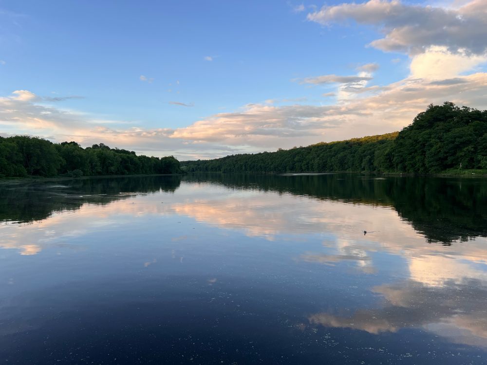 The sky reflecting on a river in Maine with trees along both shores 