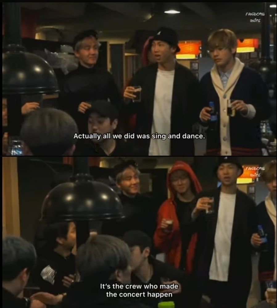 Screengrab Namjoon stands with drink in hand, as if giving a toast, V on one side, Jungkook and Hobi on the other, facing a table of guys in black t-shirts.  Text "Actually all we did was sing and dance. It's the crew who made the concert happen."