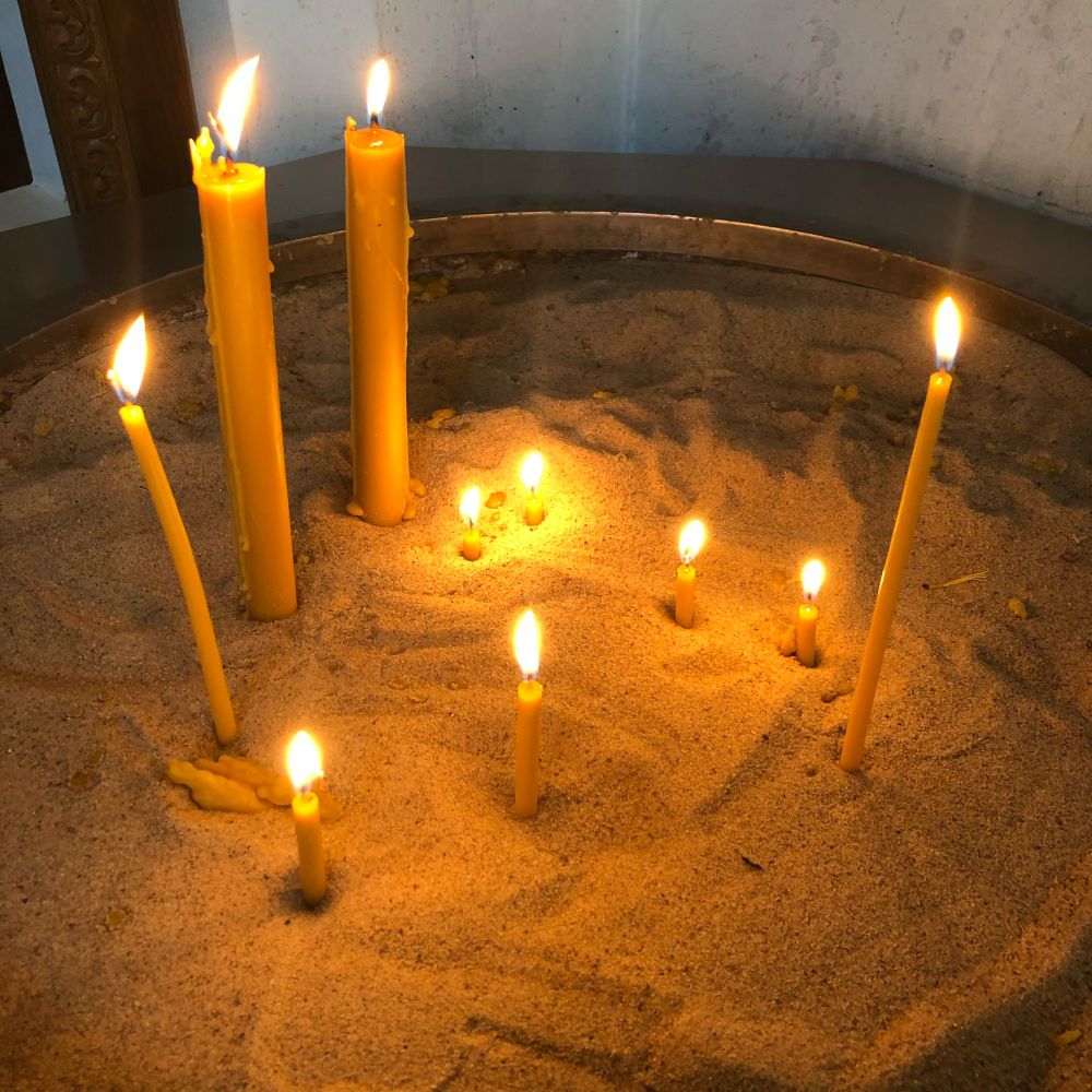 Several candles of various heights and thicknesses are standing in a sand-filled vessel of some kind. 