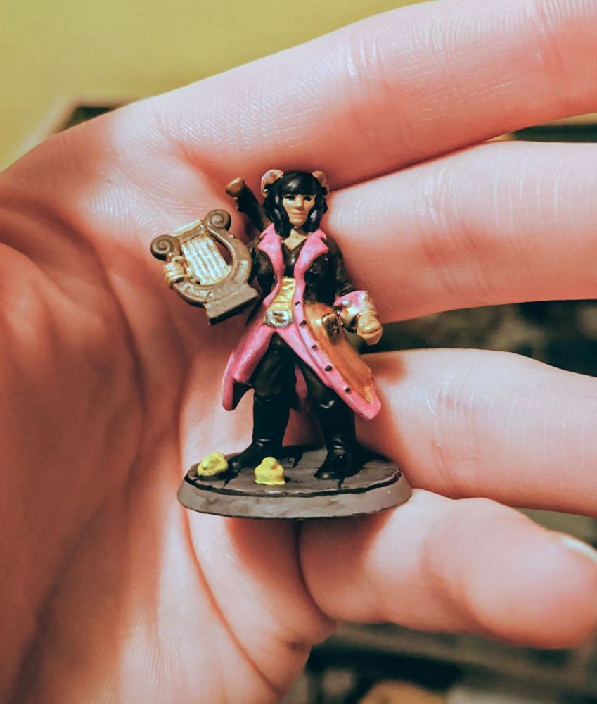Heroforge tiefling bard wearing a pink and black coat, on the floor around them are two yellow rubber ducks. 