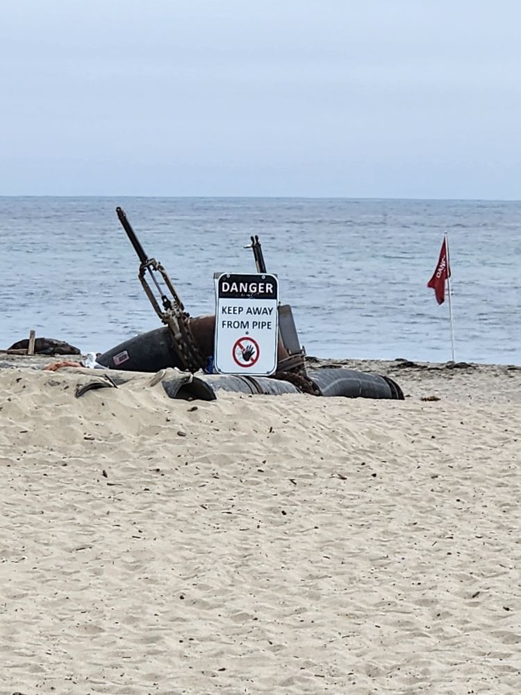 Sign on beach reading "DANGER KEEP AWAY FROM PIPE"