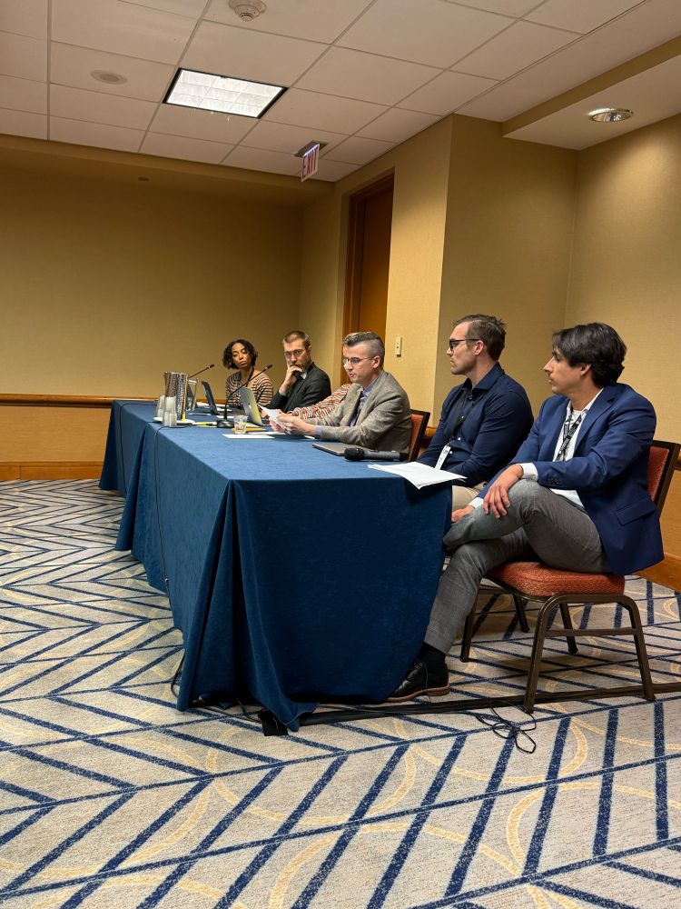Presenters discuss their dissertation research seated at a long table in a conference room