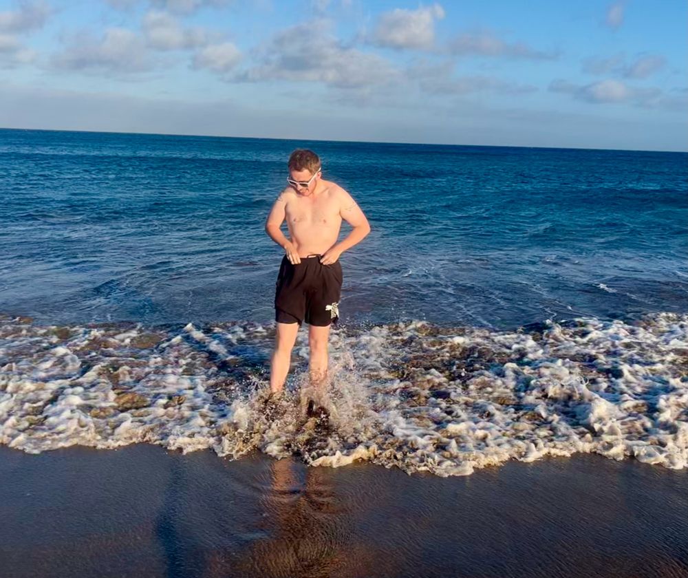 Arthur in the sea in a pair of black shorts and sunglasses