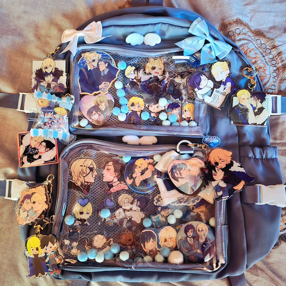 Blue backpack style ita bag with various dimilix pins and charms as well as blue and white bows and pompoms.