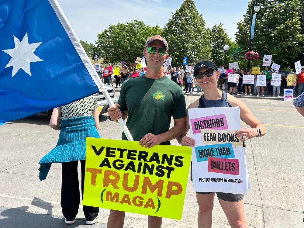 Man holding a sign that says veterans against Trump. Woman holding a sign that says dictators fear books more than bullets 