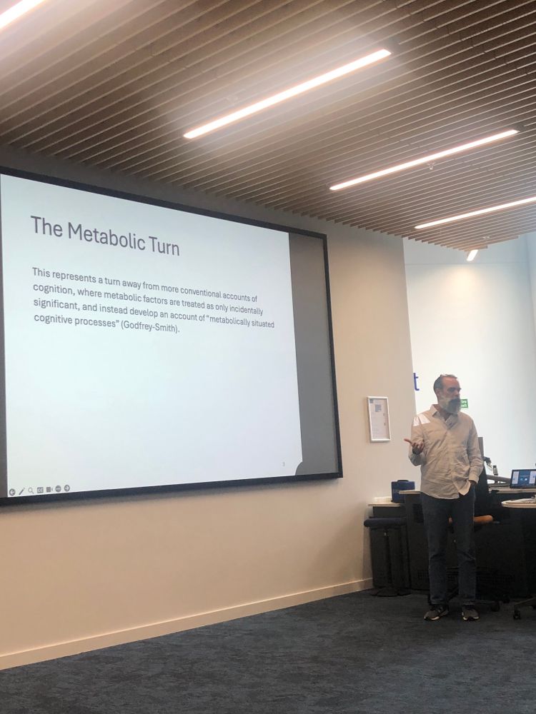 Philosopher Patrick McGivern, wearing a white shirt and blue jeans, explaining the „metabolic turn“, i.e. the importance of metabolism for understanding cognition