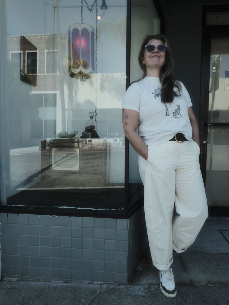 A woman in white pants and a white T-shirt with sunglasses on leans against a window and it’s my friend. It’s not a stranger so there.