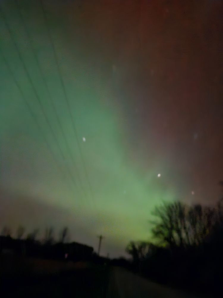 Night sky with dark horizon and Aurora Borealis showing purple and green swathes of light like clouds.