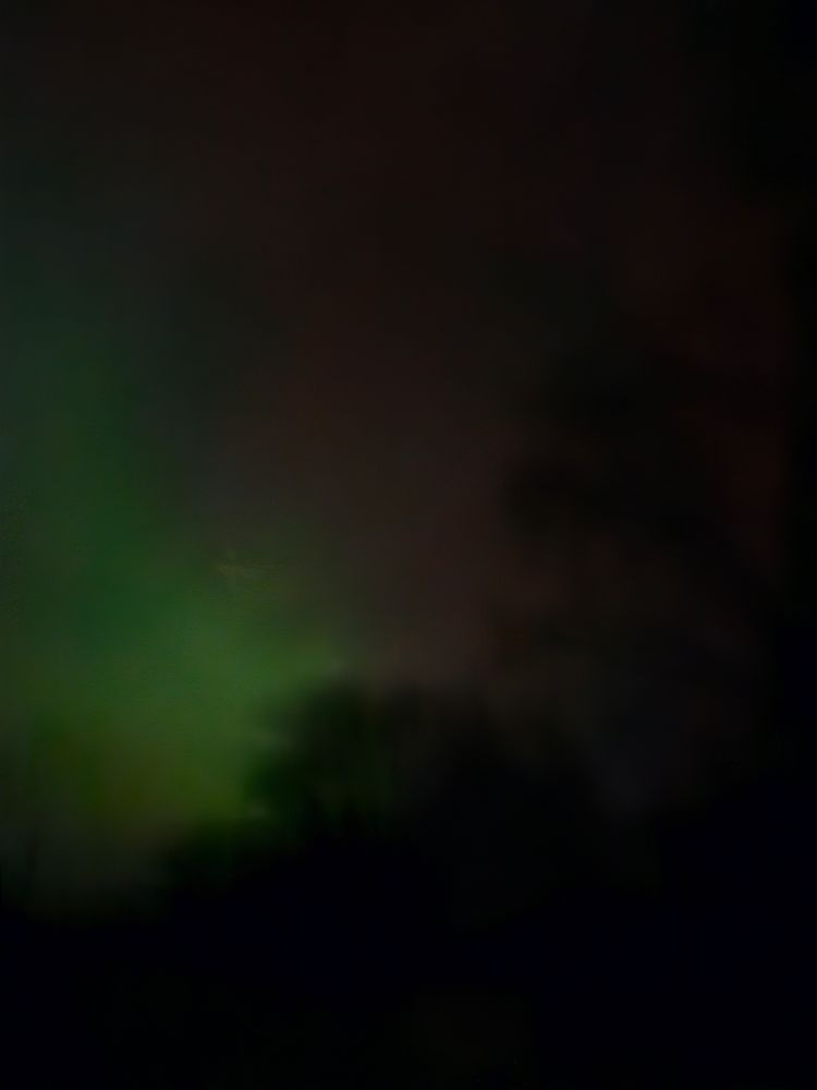 Night sky with dark horizon and Aurora Borealis showing purple and green swathes of light like clouds.