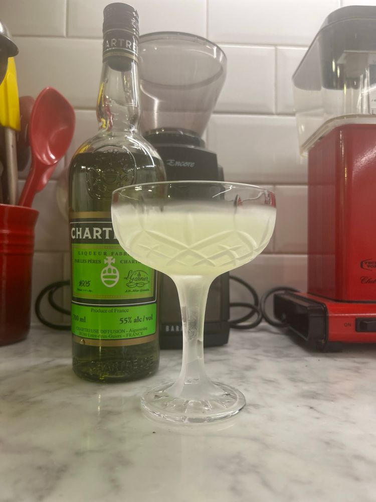 Immigt cocktailglas med en jättegod ljusgrön blandning. Lite köksprylar och en spritflaska i bakgrunden