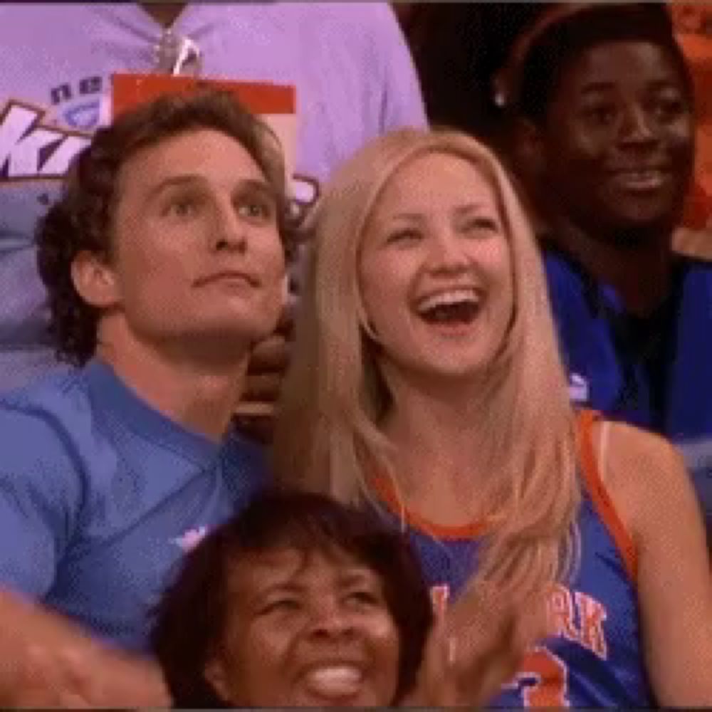 a group of people are sitting in a stadium watching a game and one of them is wearing a knicks jersey .