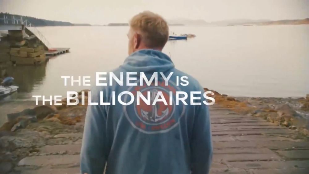 a man in a blue hoody looks out on a calm body of water