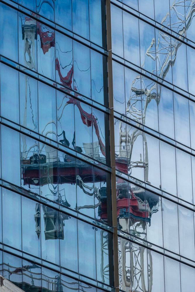 Color photograph of a construction crane tower reflected in the glass panes of a high rise building in Detroit. 