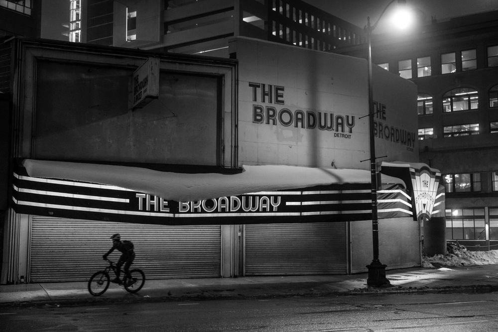 Black-and-white photograph taken at night of a bicycle silhouetted against a shuttered store called the Broadway.