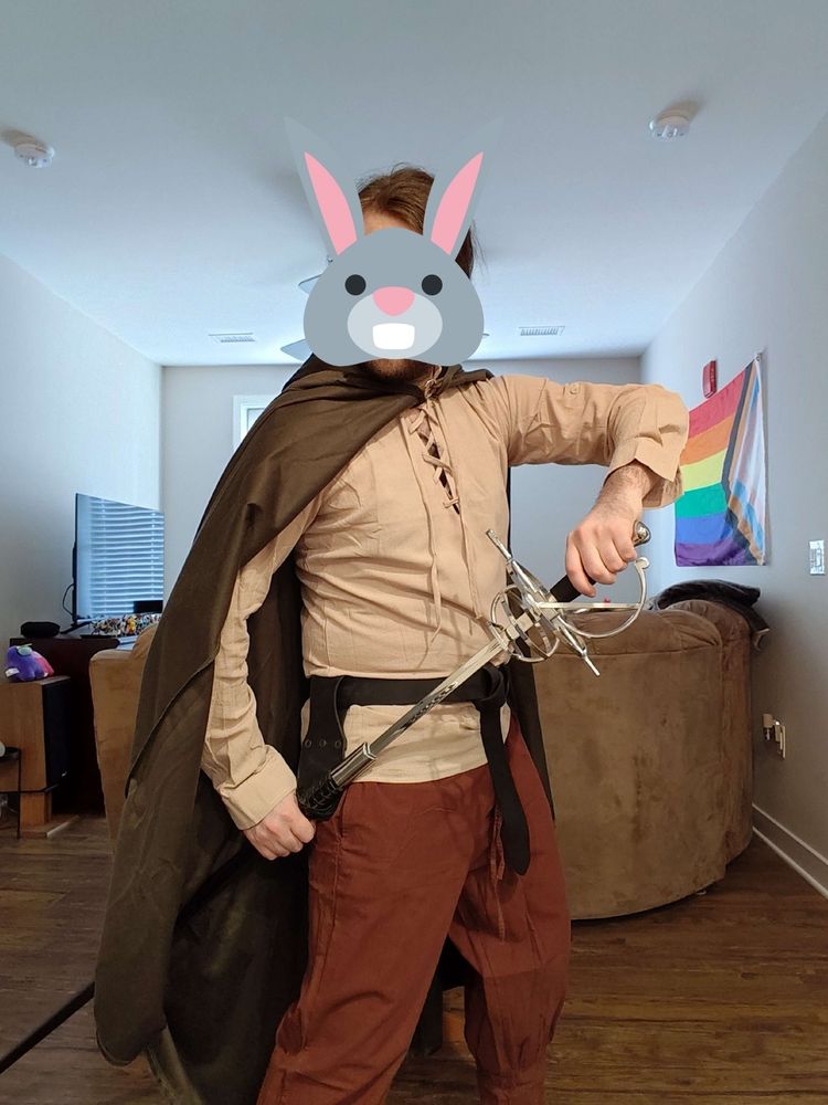A man with a rabbit emoji obscuring his face, wearing a cloak half-slung over his shoulder like a cape, halfway drawing a rapier