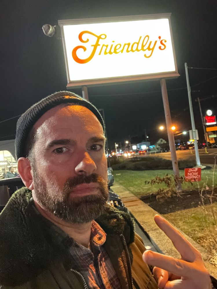 A middle-aged man poses in front of an illuminated Friendly’s sign