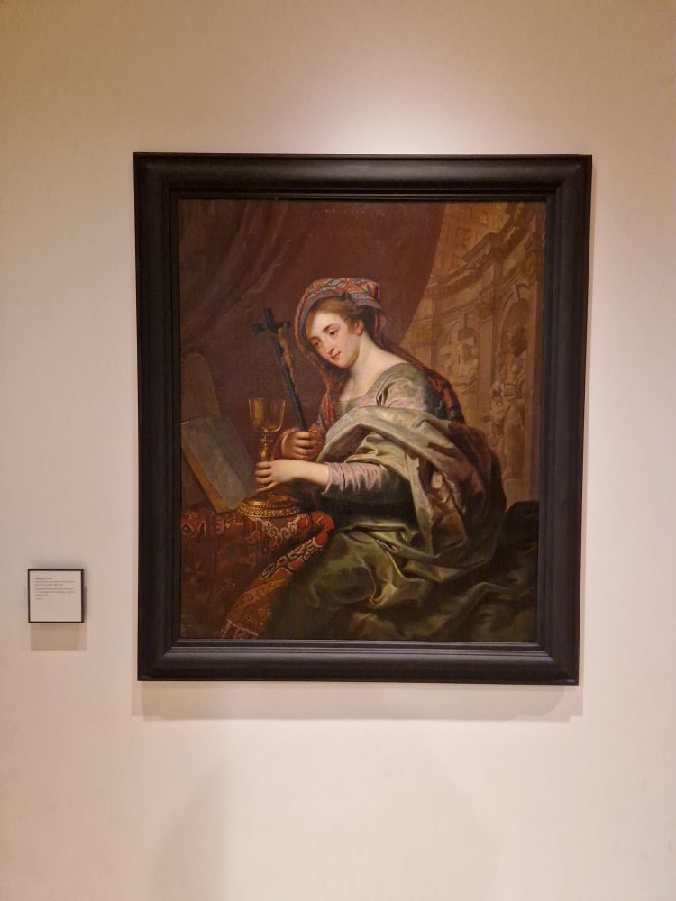 A painting displayed in the Ashmolen Museum in Oxford. It shows a woman holding a chalice and a cross or crucifix.