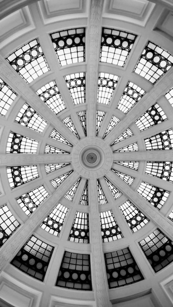 Photograph taken looking up at the central point of a circular glass domed ceiling in Lady Lever Art Gallery, Port Sunlight, The Wirral. 

Sixteen repeated slices of glass intersected by masonry arms and bands. The glass had a turquoise hue and features decorative circles in the leadwork. Original photograph turned monochrome for impact.