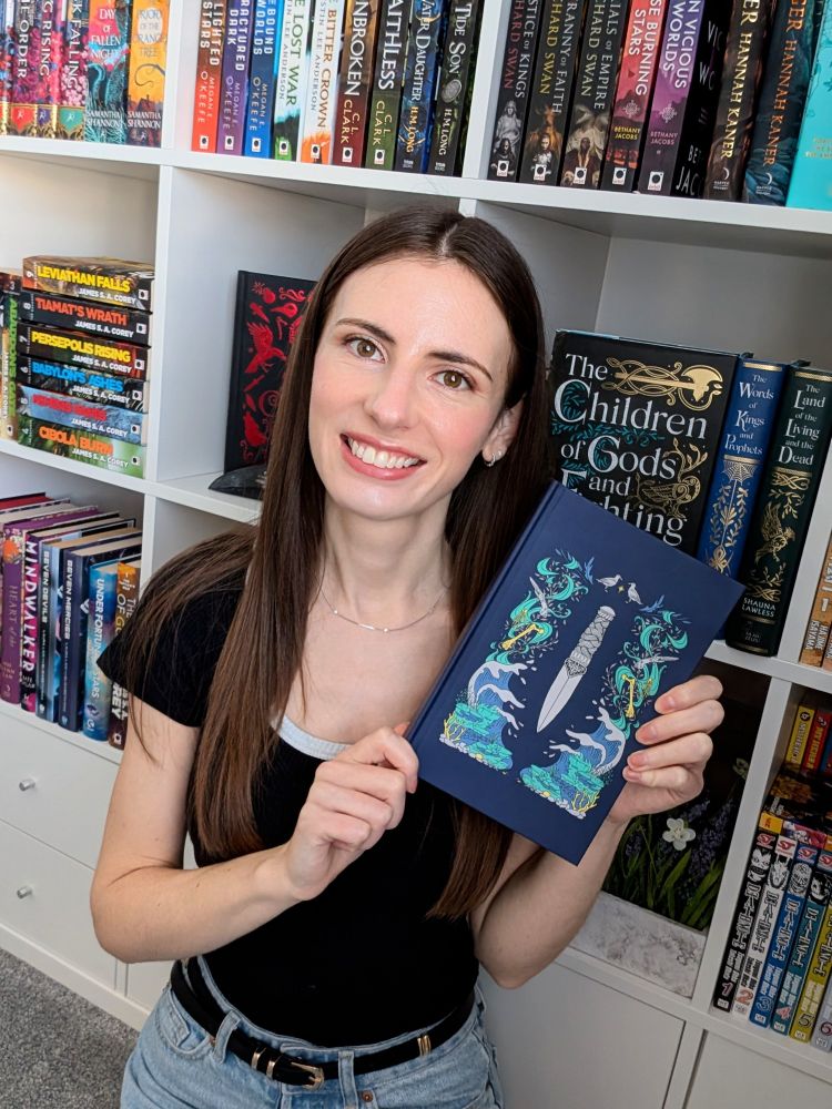 N. C. Scrimgeour in front of a bookshelf, holding an illustrated hardcover copy of her new book, Mists of Memory 