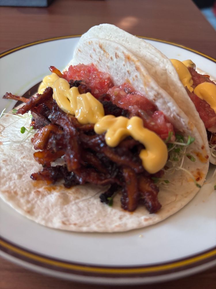 Lautasella kaksi pehmeää tacoa joiden täytteenä silmusalaattia, nyhtösientä, itse tehtyä tuoretomaattisalsaa ja poppiksen tacocheddarkastiketta.