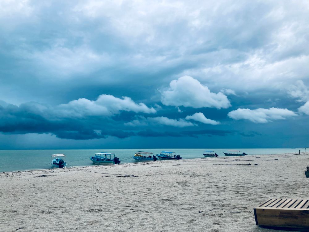 Celestún beach in Merida. Six small boats are docked at the shoreline. The aqua sea is flanked by storm clouds. 