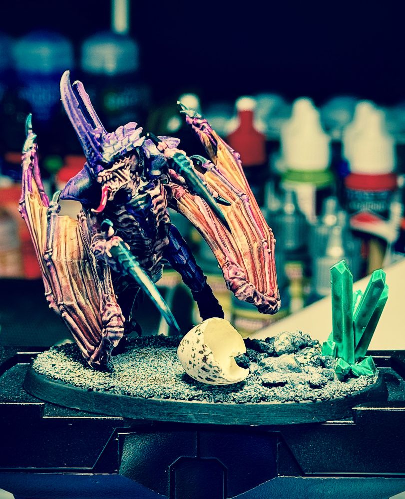 Winged tyranid prime mounted on a dark base with green crystals on the right. There's an  eggshell in the foreground of the base. (A swallow eggshell actually 😉) 