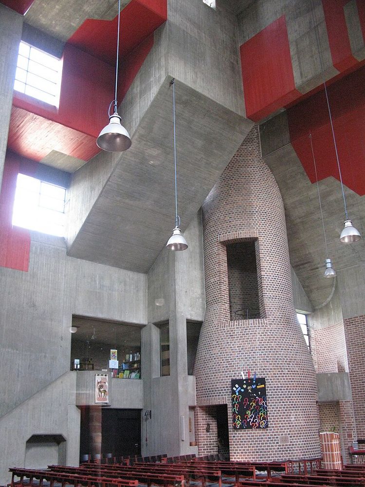 Interior showing a rounded brick tower that looks like a chimney. The ceiling is of concrete with swathes painted red. Just out of shot to the right is the altar. Photo by Andreas Schwarzkopf via Wikimedia Commons. 