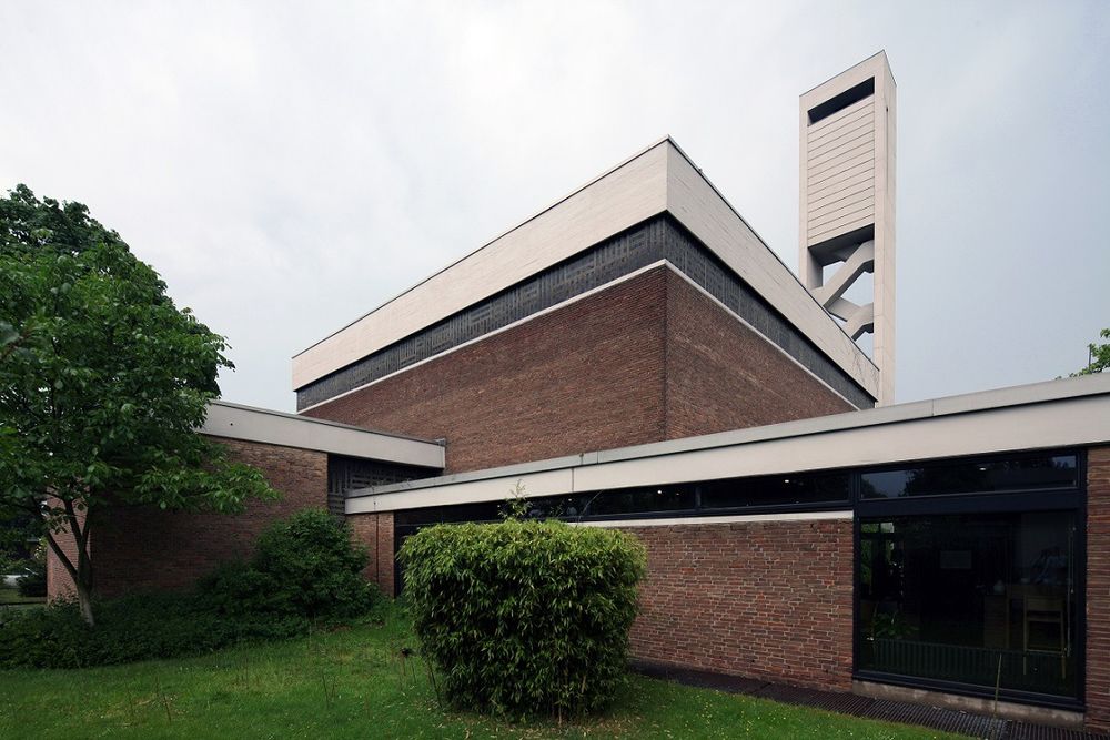 A church building with lots of different planes. The main building is made of red brick but has an extensive CIP concrete fascia; in between these two surfaces is a narrow band of clerestory windows. The main worship space is nearly cubical; in front are two lower spaces. In the back is a rectangular concrete church tower. Photo by Jürgen Wiener and Michaela Kalusok via Straße der Moderne, https://strasse-der-moderne.de/kirchen/krefeld-bockum-christuskirche/