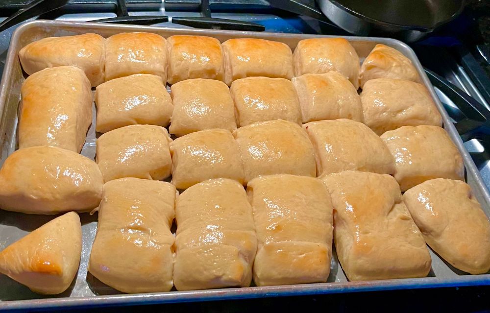 Hand made dinner rolls of varying shapes and sizes on a metal baking sheet.