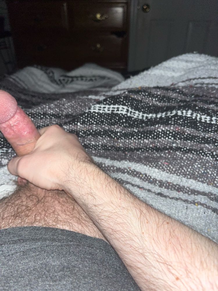 A male lying on a bed gripping his penis 
