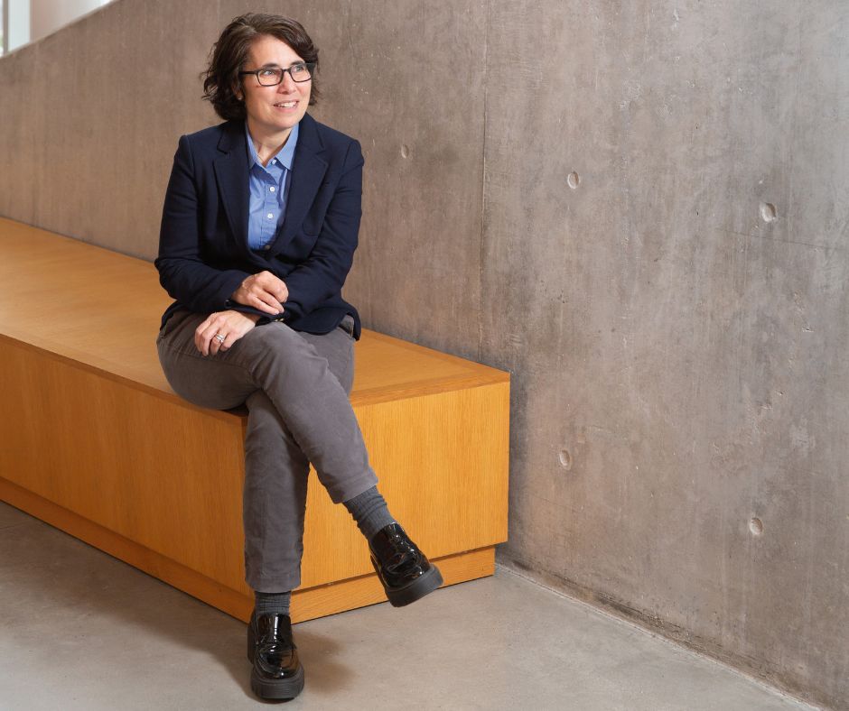 Cherie Kagan sitting on a bench, legs crossed, smiling