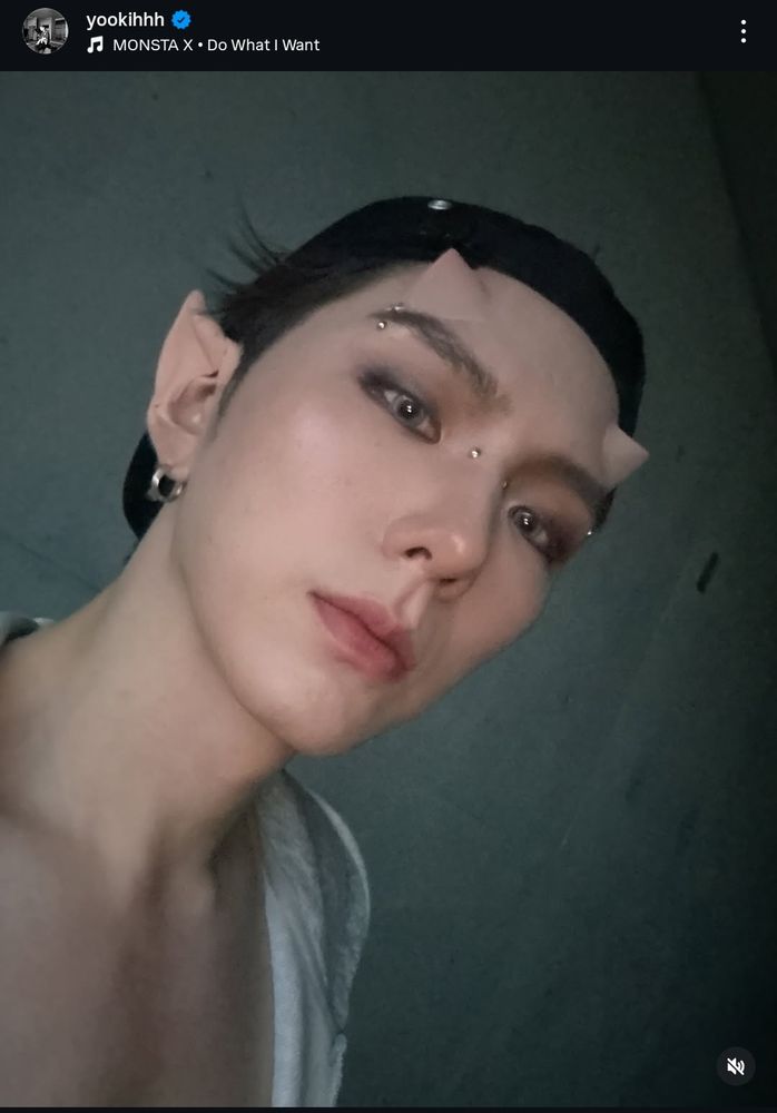 integrante do grupo de kpop monsta x, yoo kihyun, com lentes de contato verdes, piercings falsos na ponte do nariz e nas sobrancelhas, e próteses de silicone imitando uma orelha de elfo e dois chifres, da cor da pele do artista