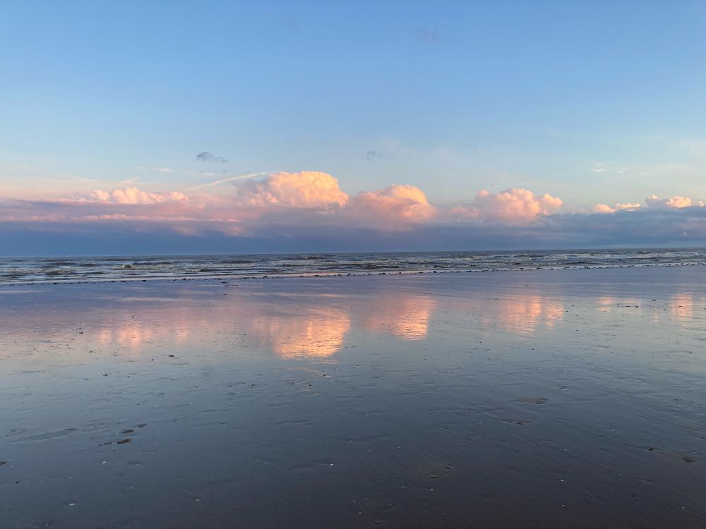 Pink fluffy clouds reflected on the wet beach