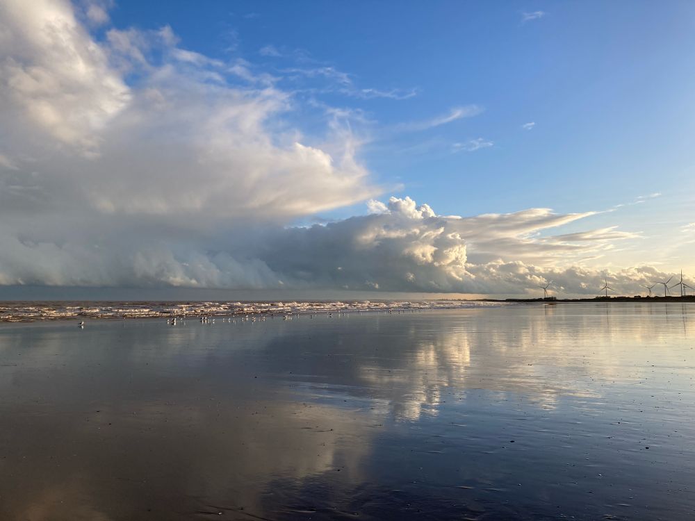 Dramatic clouds with some blue sky reflected on the wet beach
