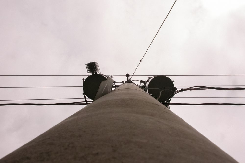Looking up at a utility pole with circular attachments and cables against a cloudy sky