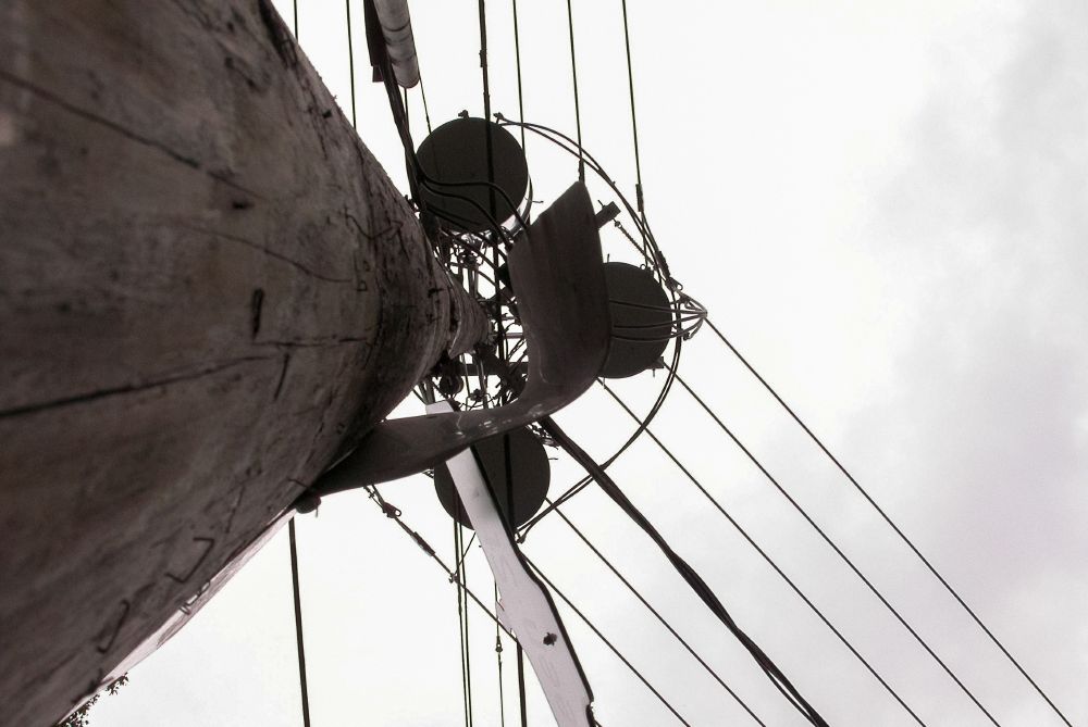 Low-angle view of a tall wooden utility pole with wires extending outward against a cloudy sky.