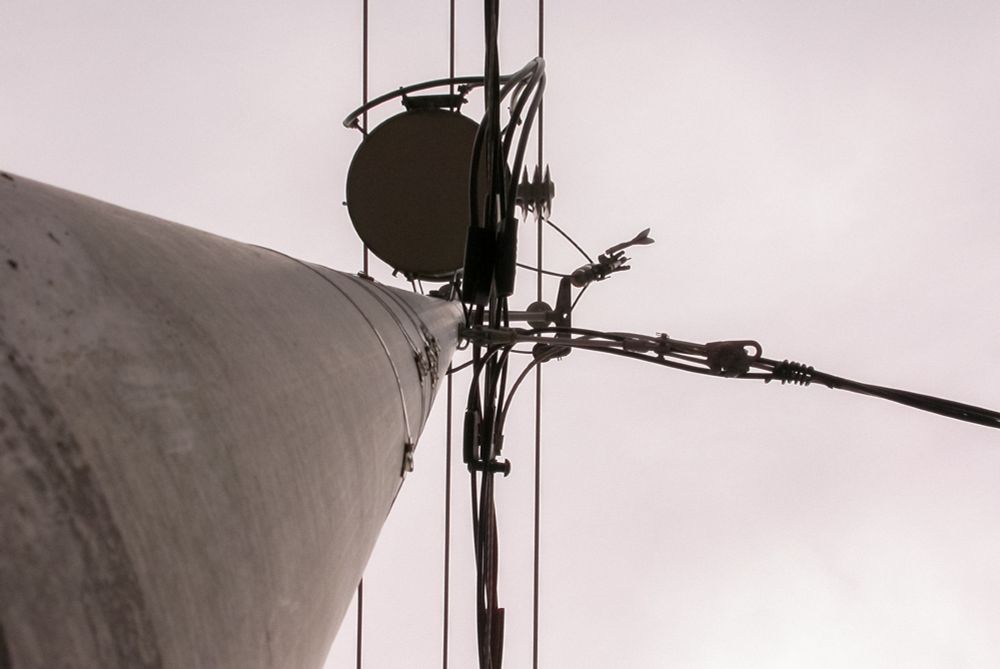 Looking up at a utility pole with circular attachments and cables against a cloudy sky