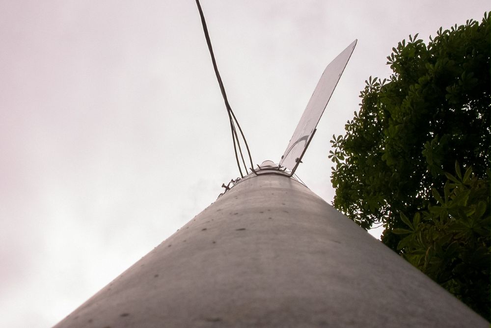 Upward view of a streetlight pole with electrical wires crossing horizontally against a pale, overcast sky.