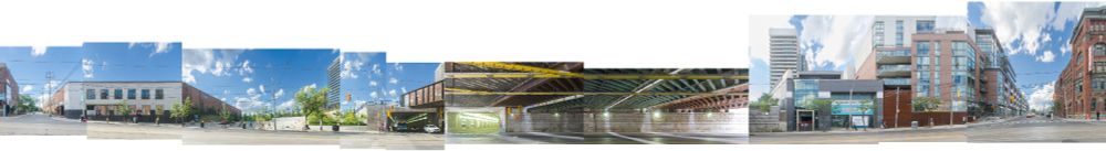Panoramic cityscape with modern and historic buildings under a bright blue sky. Both sides of a rail underpass are shown, and angled glimpses of a traffic tunnel.