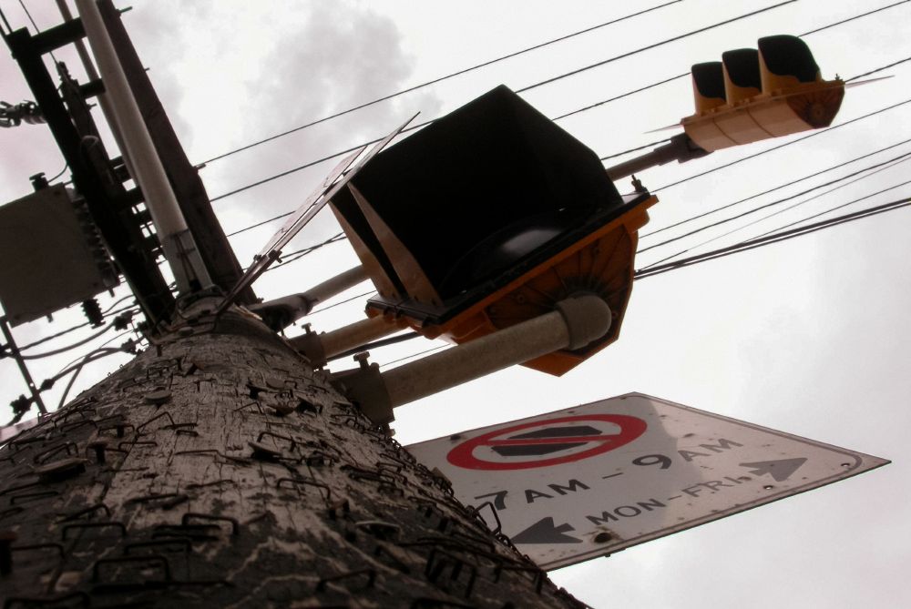 Low-angle view of a tall wooden utility pole with wires extending outward against a cloudy sky.