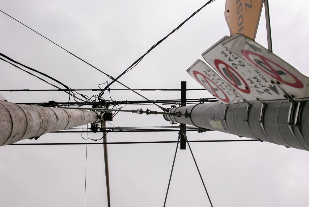 Upward view of two tall utility poles with interconnected power lines against a cloudy sky.