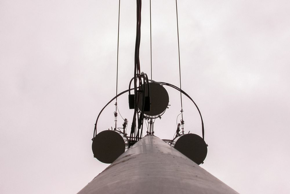 Looking up at a utility pole with circular attachments and cables against a cloudy sky