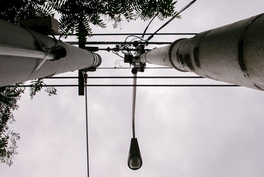 View from below of two utility poles with wires and transformers against an overcast sky. 