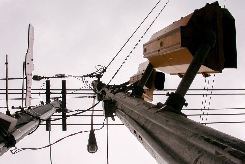 View from below of two utility poles with wires and transformers against an overcast sky. 
