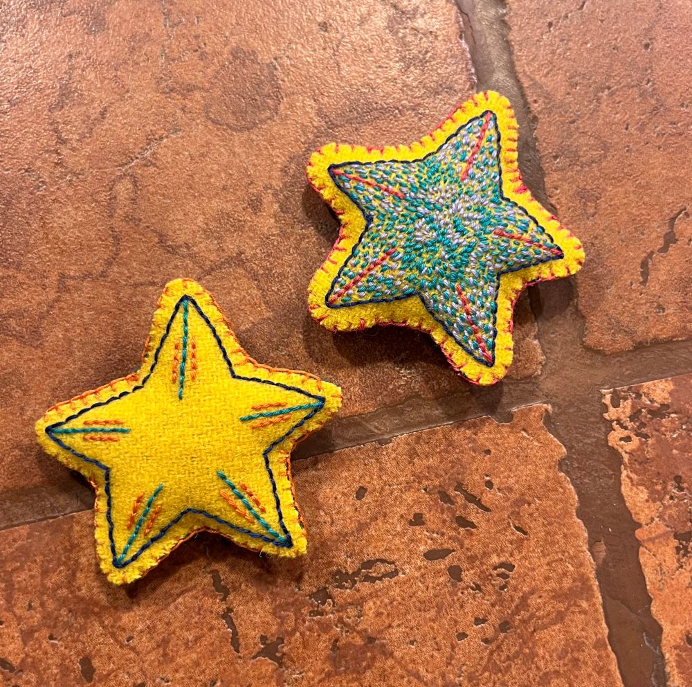 two more yellow felt stars; one is quite simple, bearing a few stripes. the other is host to a multitude of tiny purple stitches.
